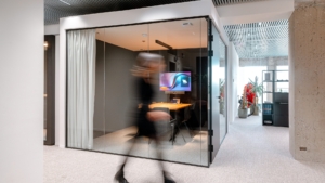Photo of a woman walking in an office. She is walking past a meeting room
